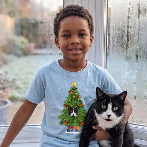 Boy by a frosty window holding his cat, wearing a light blue kids' Christmas tree pet photo t-shirt